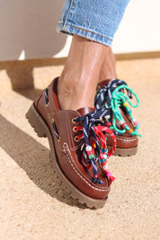 Andie boat shoes close-up — tan leather chunky sole boat shoe with multicolour handcrafted beaded laces in navy, red and teal, worn on body with jeans, handcrafted in Portugal by Alameda Turquesa