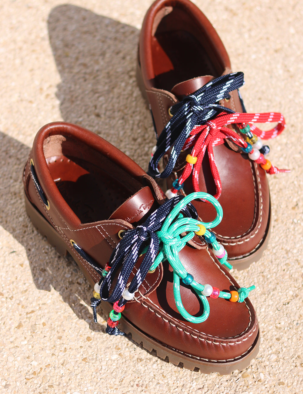 Andie boat shoes flat lay — tan leather chunky sole boat shoes with multicolour handcrafted beaded laces in navy, red and teal, shot on sand, handcrafted in Portugal by Alameda Turquesa