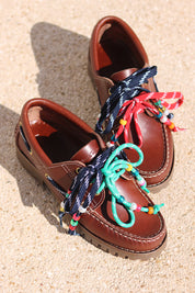 Andie boat shoes flat lay — tan leather chunky sole boat shoes with multicolour handcrafted beaded laces in navy, red and teal, shot on sand, handcrafted in Portugal by Alameda Turquesa