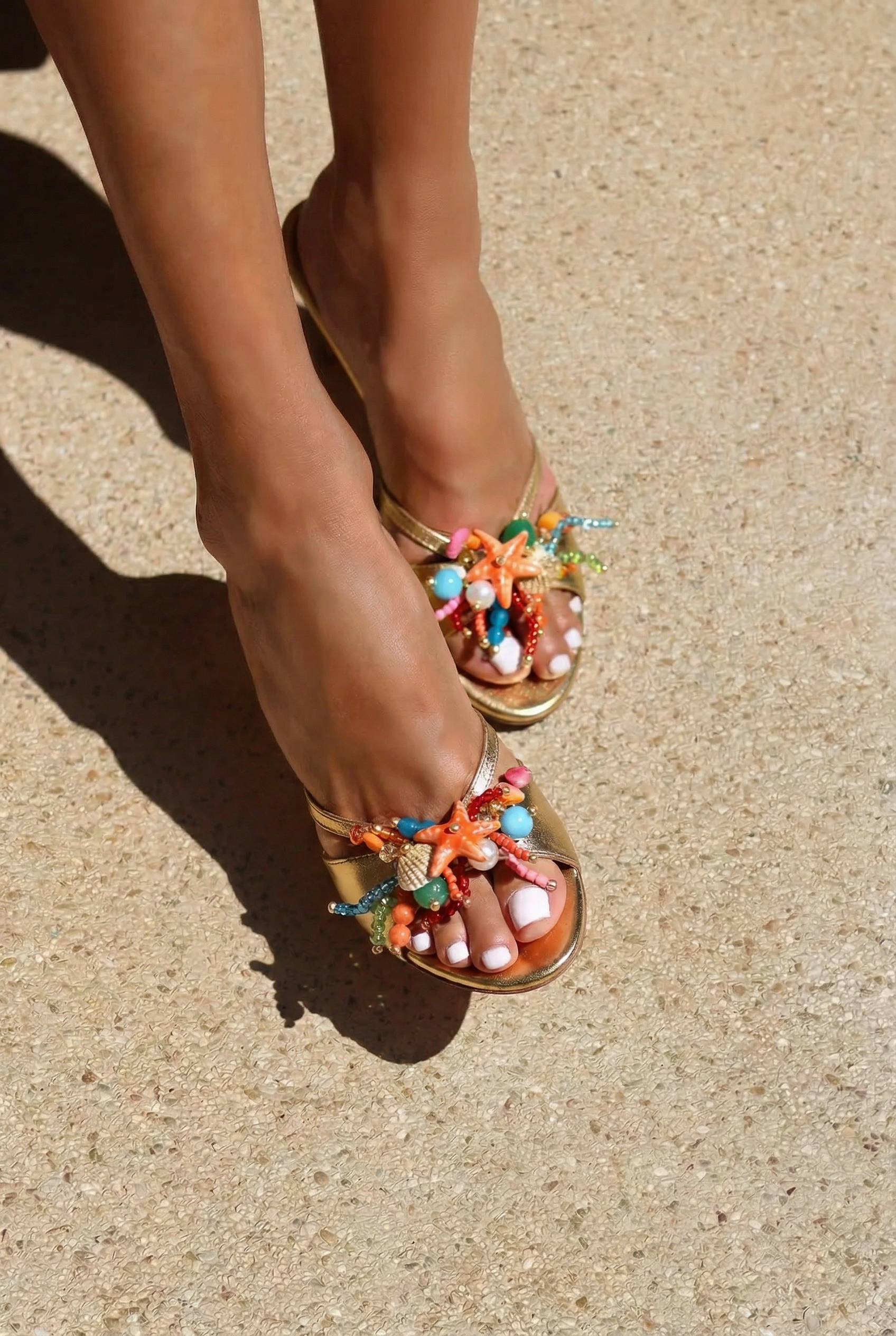 Bahamas mules close front view on both feet — gold leather mid-heel open-toe mules with hand-painted starfish, natural shells, pearl and multicolour bead embellishments in coral, turquoise and pink, shot in sunlight on sand, handcrafted in Portugal by Alameda Turquesa