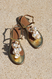 Belize sandals flat lay on sand — gold leather toe-post flat sandals with hand-applied oversized pearls and natural shell embellishments, Alameda Turquesa leather insole, handcrafted in Portugal by Alameda Turquesa