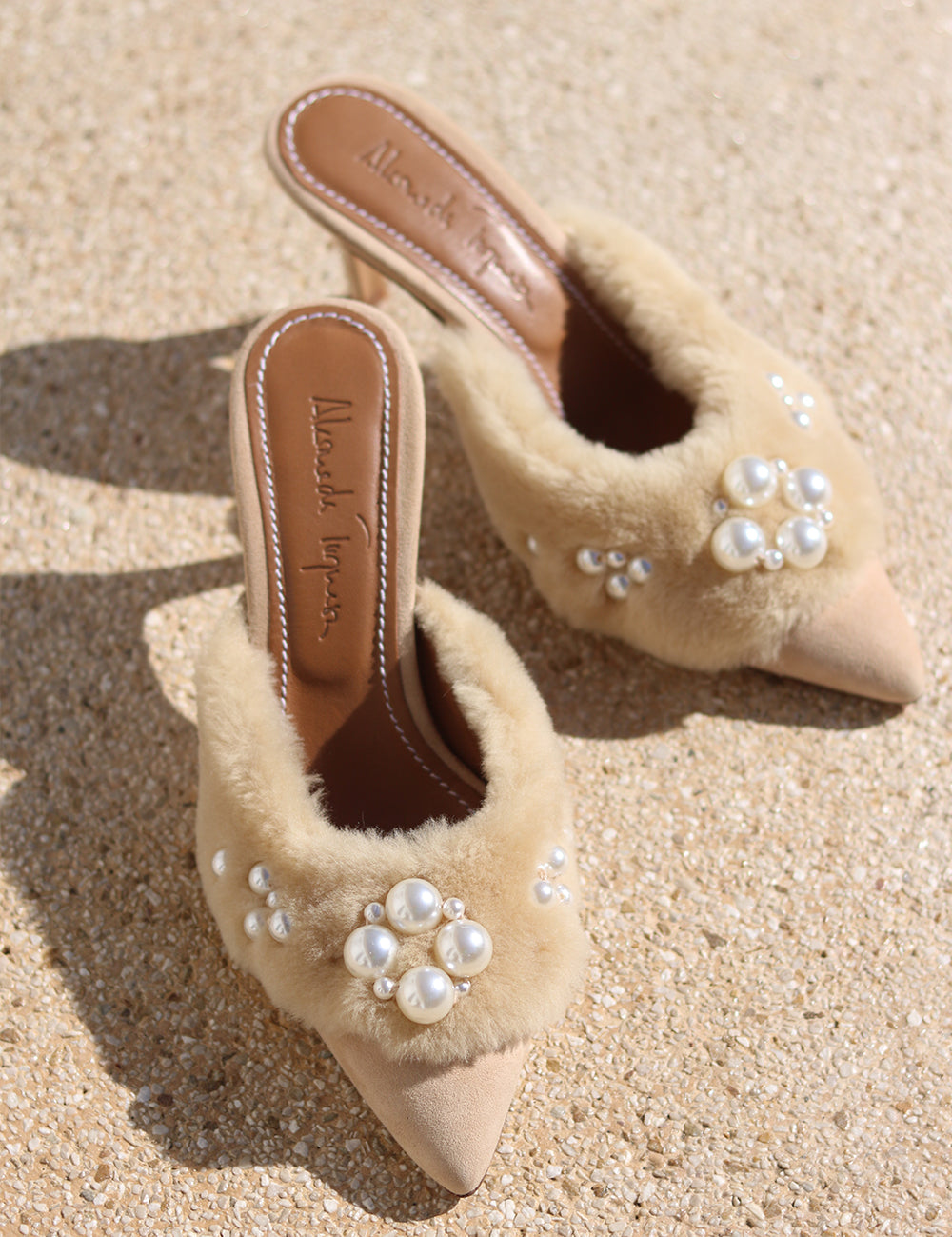 Bella shearling mules flat lay — cream shearling pointed-toe stiletto mules with hand-applied pearl cluster embellishments, shot on sand, handcrafted in Portugal by Alameda Turquesa