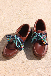 Ben chunky leather boat shoes flat lay — tan leather boat shoes with handcrafted turquoise and multicolour beaded laces on sand, luxury shoes by Alameda Turquesa Portugal
