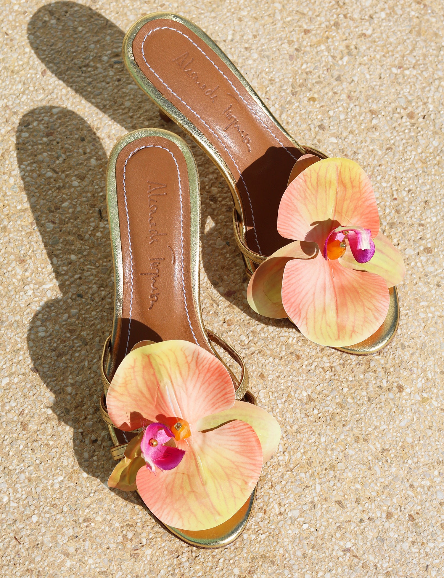 Cecily Gold mules flat lay — gold stiletto heels with oversized handcrafted orchid embellishments in peach, coral and fuchsia, tan leather insole with Alameda Turquesa branding, handcrafted in Portugal by Alameda Turquesa
