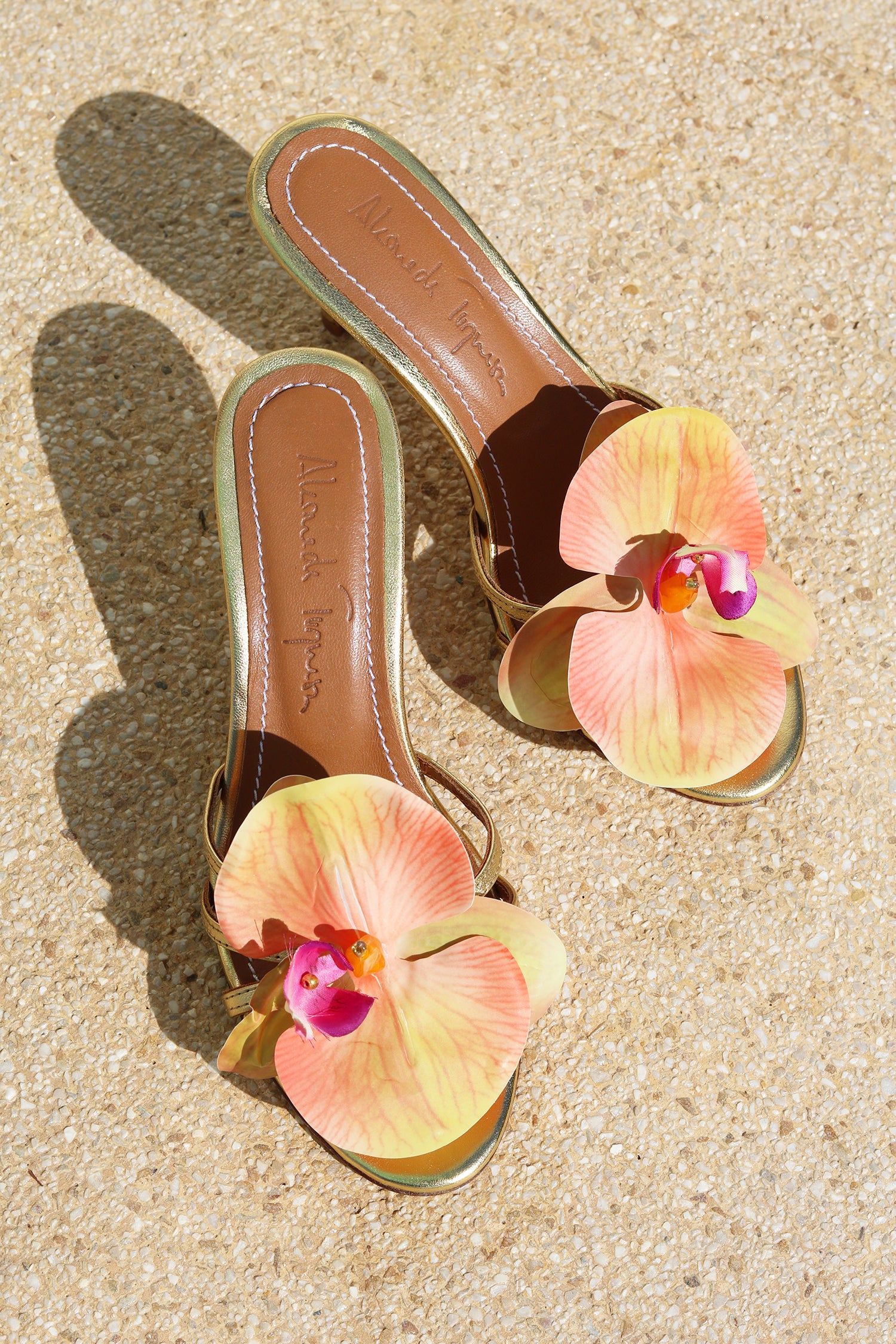 Cecily Gold mules flat lay — gold stiletto heels with oversized handcrafted orchid embellishments in peach, coral and fuchsia, tan leather insole with Alameda Turquesa branding, handcrafted in Portugal by Alameda Turquesa