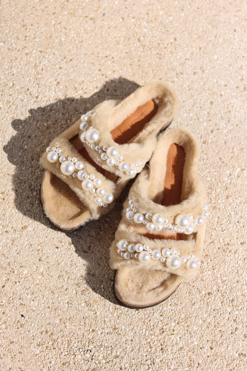 Alameda Turquesa Mimi Pearls shearling sandals with pearl embellishments, flat lay angled view on sand showing sole — as seen in Emily in Paris