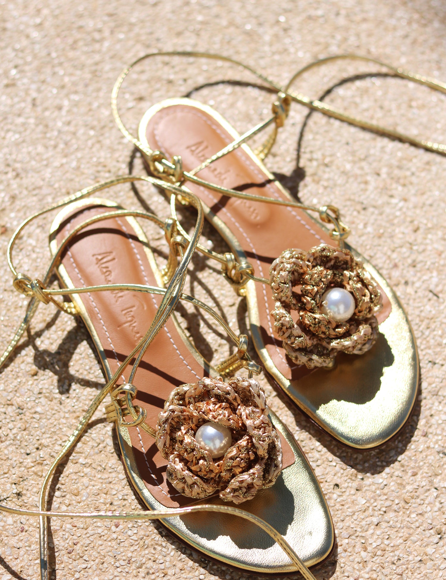 Meredith Crochet sandals flat lay — gold leather flat sandals with oversized handcrafted gold crochet rose and pearl centre, lace-up ankle wrap ties, Alameda Turquesa insole visible, shot on sand, handcrafted in Portugal by Alameda Turquesa