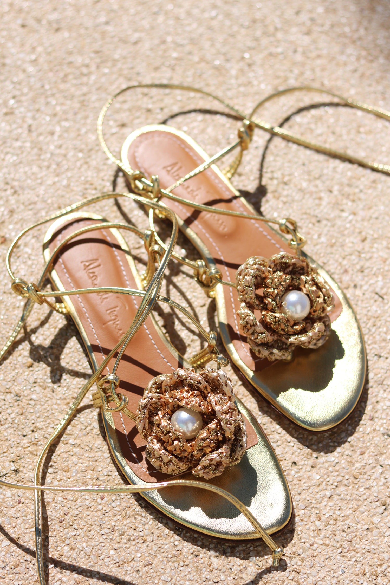 Meredith Crochet sandals flat lay — gold leather flat sandals with oversized handcrafted gold crochet rose and pearl centre, lace-up ankle wrap ties, Alameda Turquesa insole visible, shot on sand, handcrafted in Portugal by Alameda Turquesa