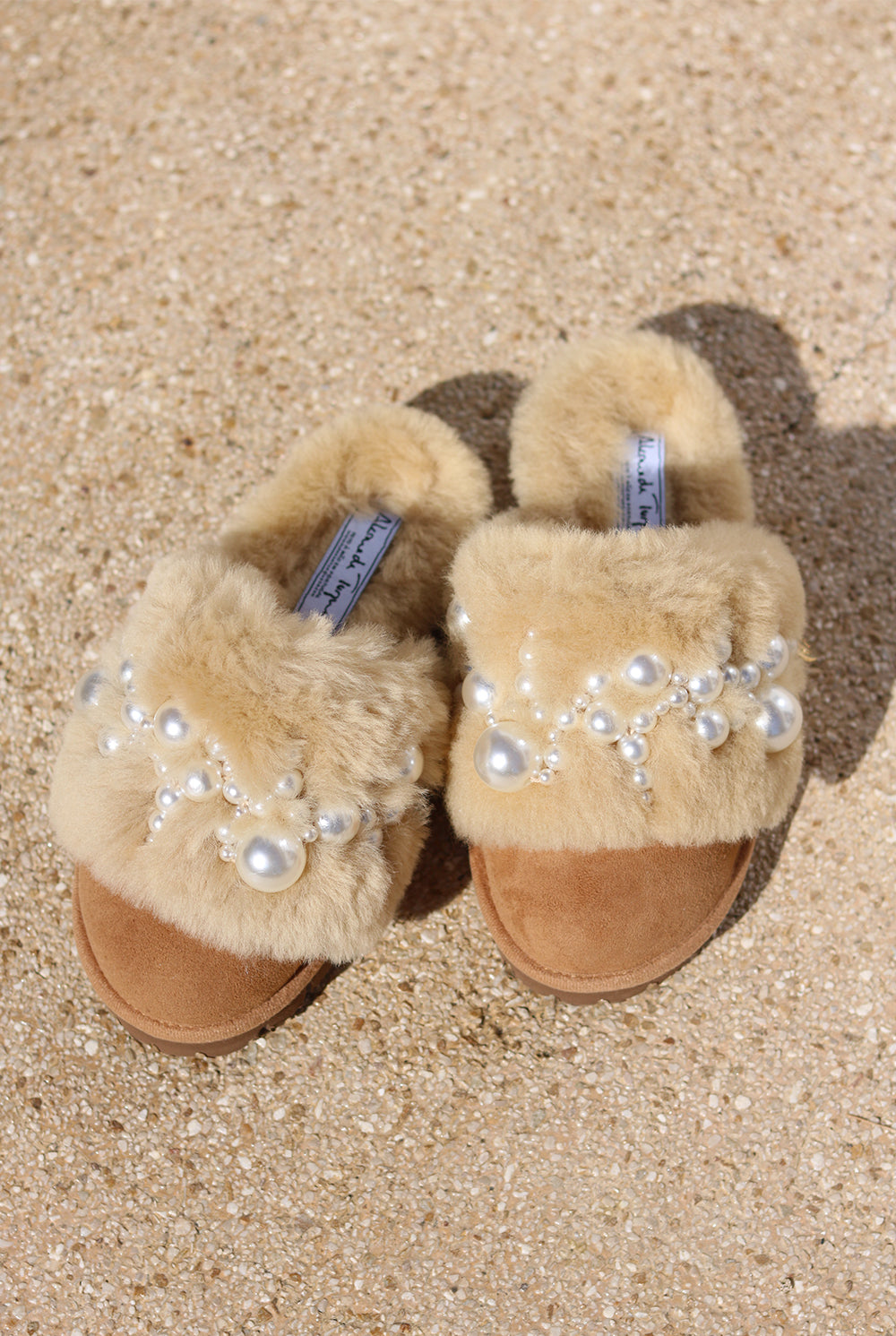 Pinctada Classic Pearls shearling mules flat lay — caramel shearling slides with hand-applied pearl embellishments on sand, Alameda Turquesa Portugal
