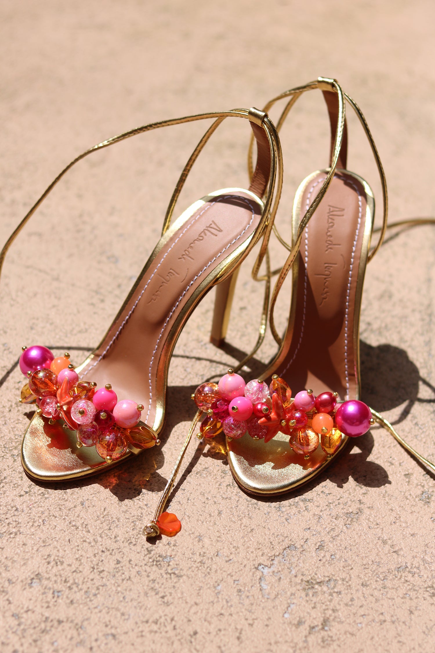 Sunkissed Coral heels flat lay — gold leather lace-up stiletto sandals with hand-applied pink pearls, coral beads and orange crystal embellishments, shot in natural sunlight, handcrafted in Portugal by Alameda Turquesa