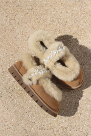Aspen Mary Jane shearling ballerina flats flat lay — cream shearling upper on a chunky caramel suede sole with handcrafted white pearl mary jane strap, single shoe styled overhead on sandy ground, handcrafted in Portugal by Alameda Turquesa