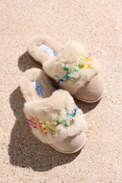 Pinctada Vanilla Rainbow shearling mules flat lay — pair of ivory shearling mules with handcrafted rainbow pearl embellishments in pink, orange, yellow, green and aqua on sand suede, styled overhead on sandy ground, handcrafted in Portugal by Alameda Turquesa