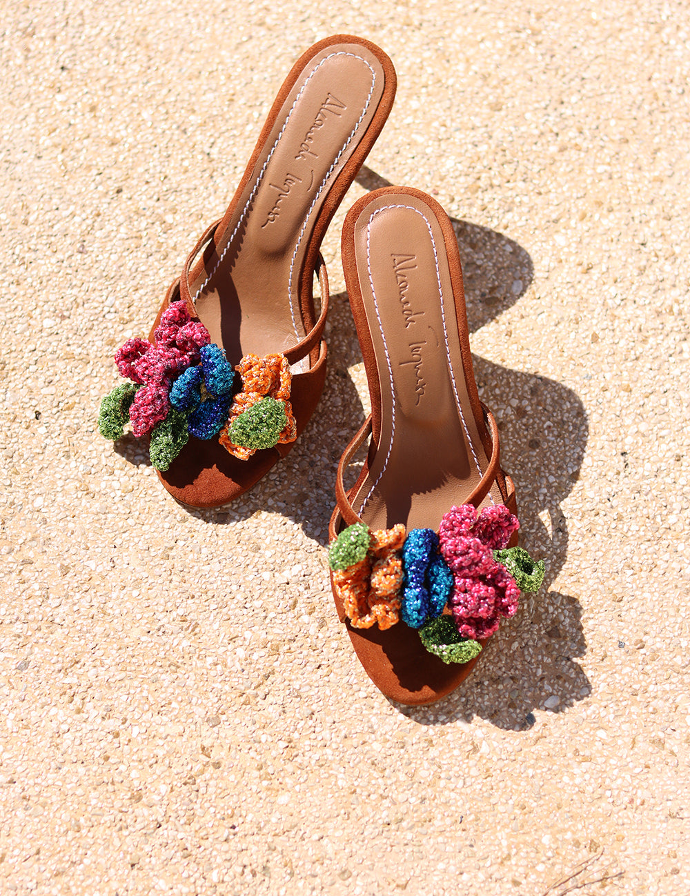 Botanica mules flat lay on sand — tan leather flat mules with handcrafted crochet flower embellishments in pink, blue, orange and green, Alameda Turquesa leather insole, handcrafted in Portugal by Alameda Turquesa