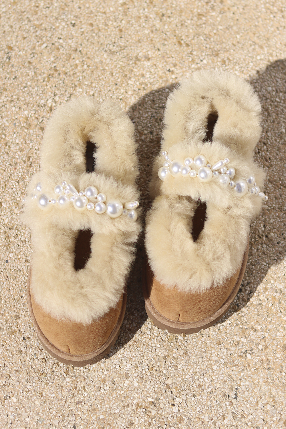 Aspen Mary Jane shearling ballerina flats flat lay — pair of cream shearling ballerinas with handcrafted white pearl mary jane straps on caramel suede, styled overhead on sandy ground, handcrafted in Portugal by Alameda Turquesa