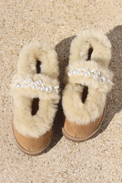 Aspen Mary Jane shearling ballerina flats flat lay — pair of cream shearling ballerinas with handcrafted white pearl mary jane straps on caramel suede, styled overhead on sandy ground, handcrafted in Portugal by Alameda Turquesa