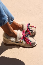 Model wearing Alameda Turquesa Lou shearling moccasins with cream genuine shearling, colourful beaded laces and chunky brown soles.