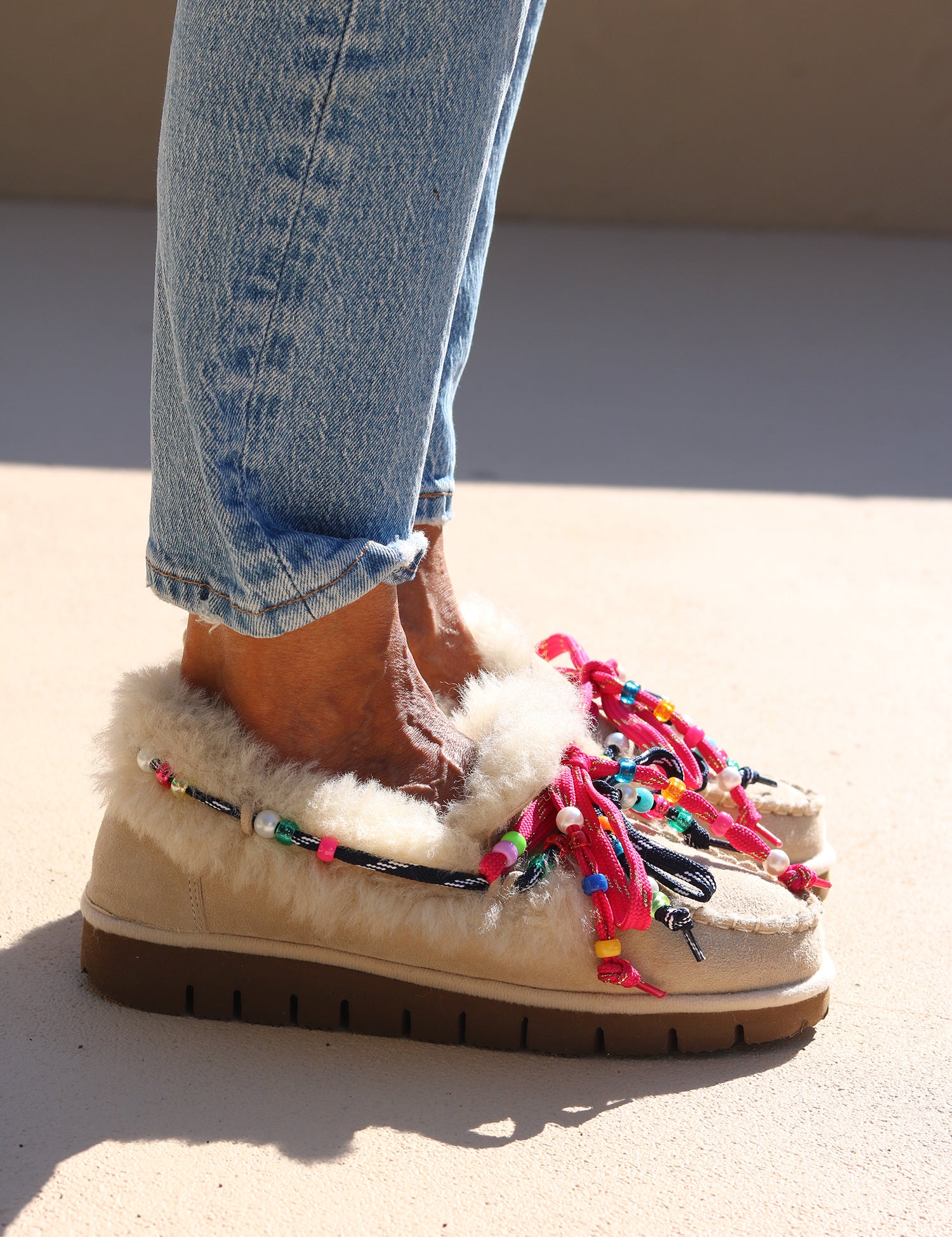 Model wearing Alameda Turquesa Lou shearling moccasins with cream genuine shearling, colourful beaded laces and chunky brown soles.