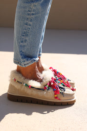 Model wearing Alameda Turquesa Lou shearling moccasins with cream genuine shearling, colourful beaded laces and chunky brown soles.