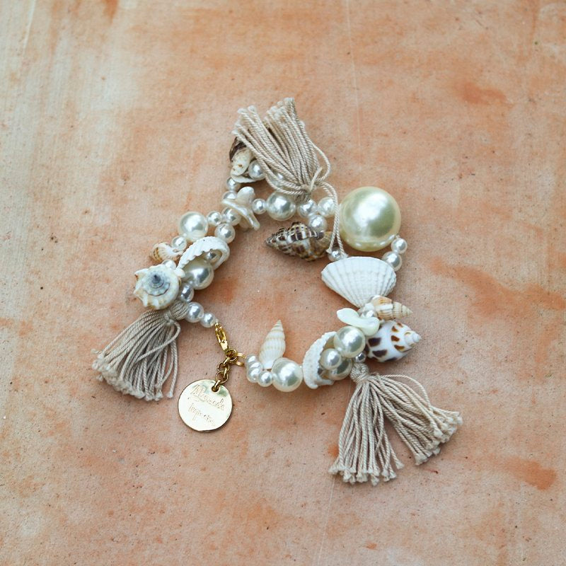 Ariel bracelet flat lay — handcrafted pearl, seashell and natural tassel bracelet with oversized pearl centrepiece, mixed shells, smaller pearls and gold Alameda Turquesa charm, shot on terracotta stone, handcrafted in Portugal by Alameda Turquesa