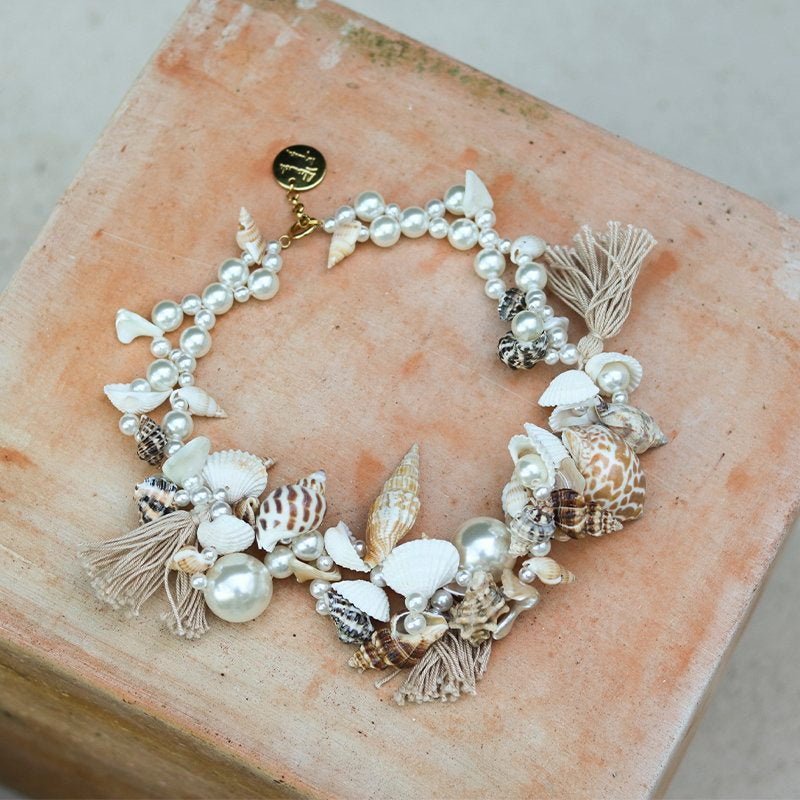 Ariel necklace flat lay — handcrafted pearl, seashell, coral and tassel necklace with gold Alameda Turquesa charm, shot on terracotta stone, handcrafted in Portugal by Alameda Turquesa
