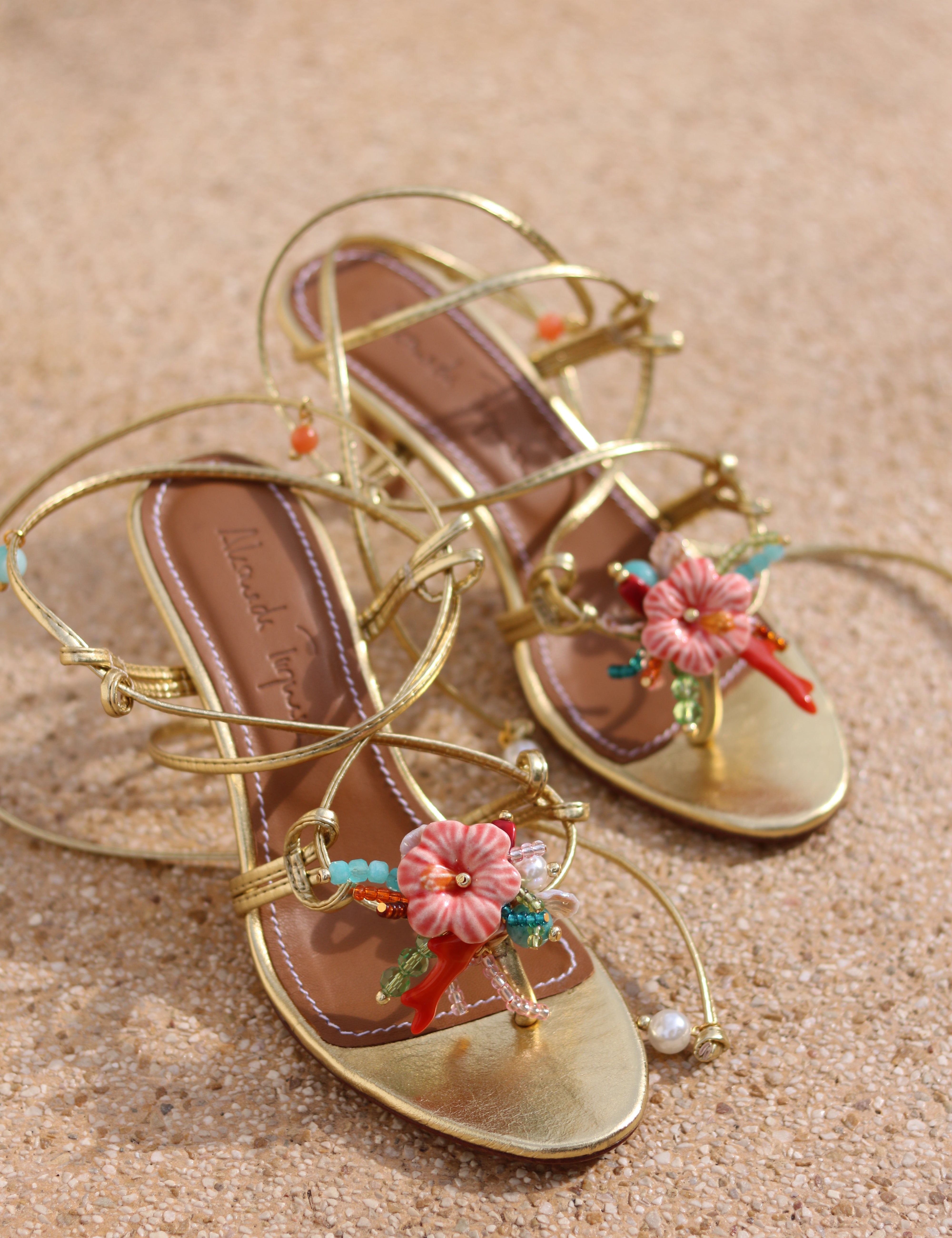 Coralie sandals flat lay, gold leather multi-strap wrap stiletto heels with hand-painted ceramic hibiscus centerpiece, turquoise and coral bead embellishments and pearl detail, handcrafted in Portugal by Alameda Turquesa