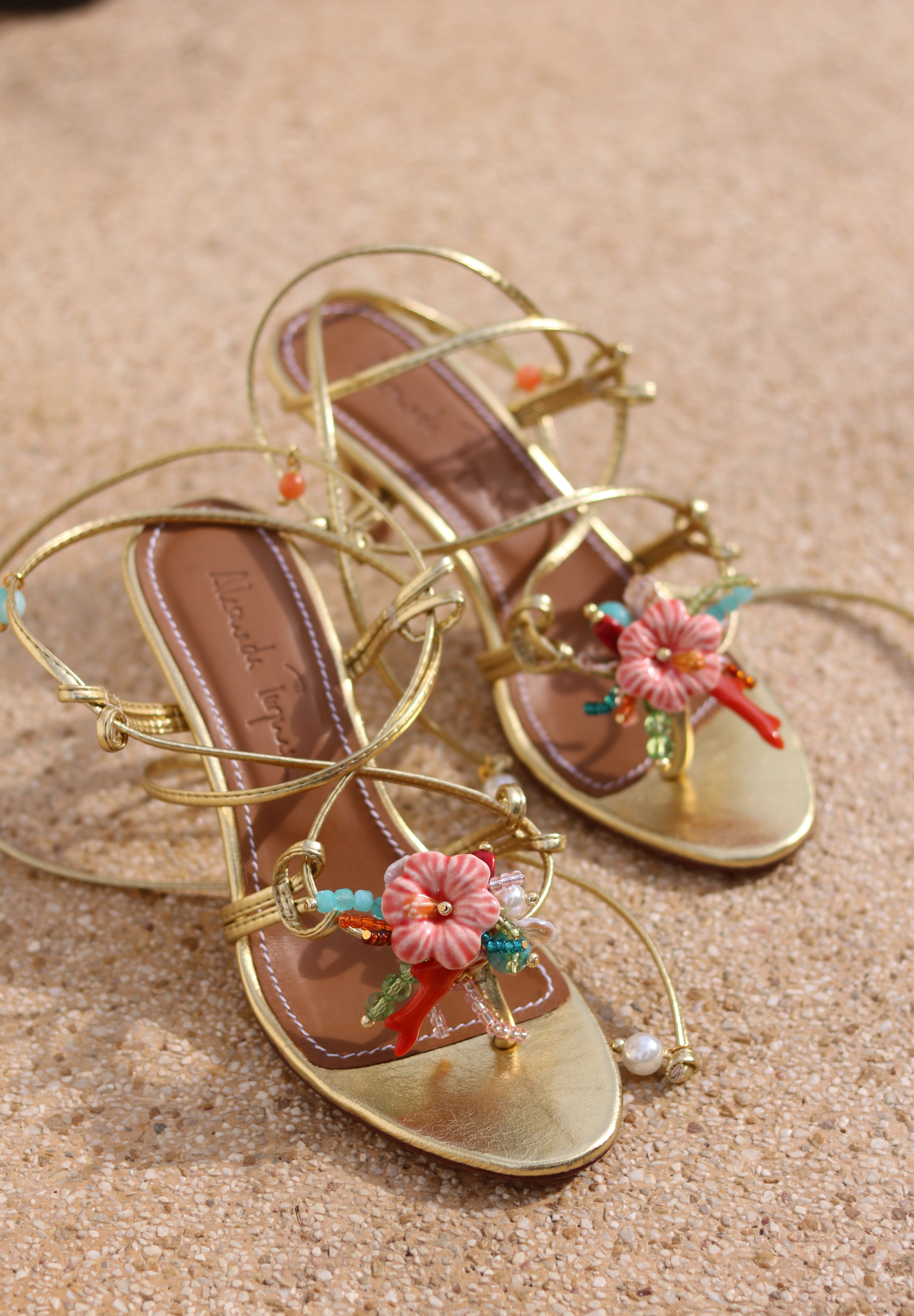 Coralie sandals flat lay, gold leather multi-strap wrap stiletto heels with hand-painted ceramic hibiscus centerpiece, turquoise and coral bead embellishments and pearl detail, handcrafted in Portugal by Alameda Turquesa