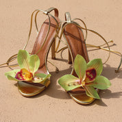 Prudence Gold flower heels flat lay — handcrafted orchid embellishment on gold stiletto sandals on sand, Alameda Turquesa Portugal